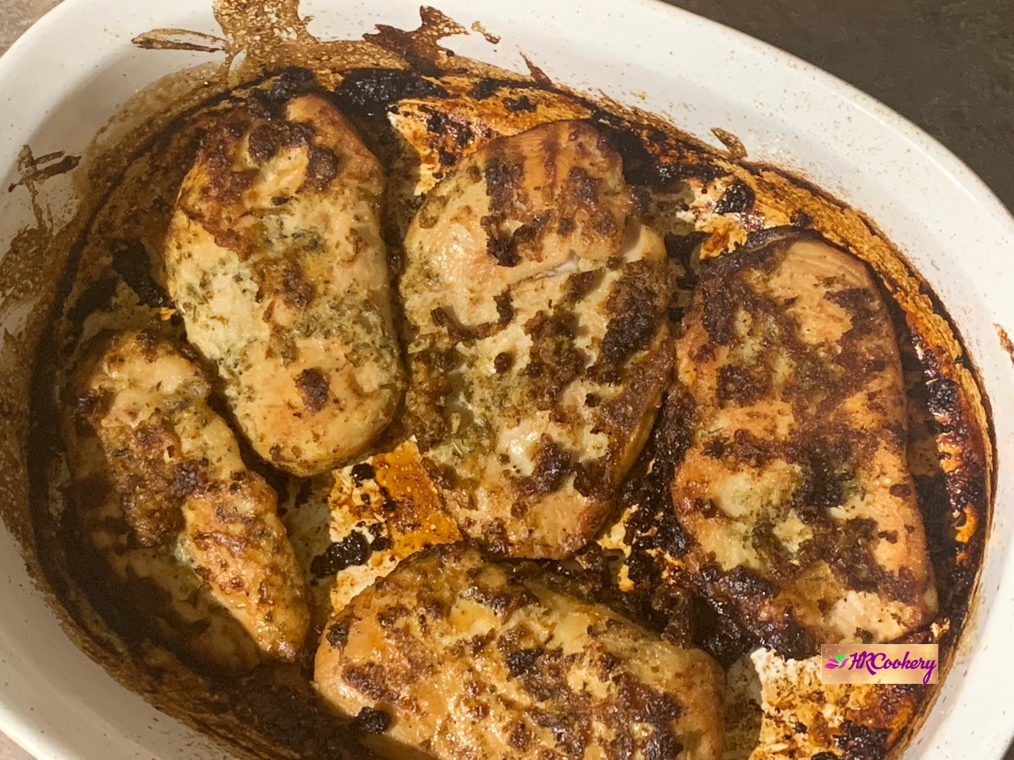 Golden baked Greek marinated chicken breasts in a casserole dish with crispy herb seasoning.