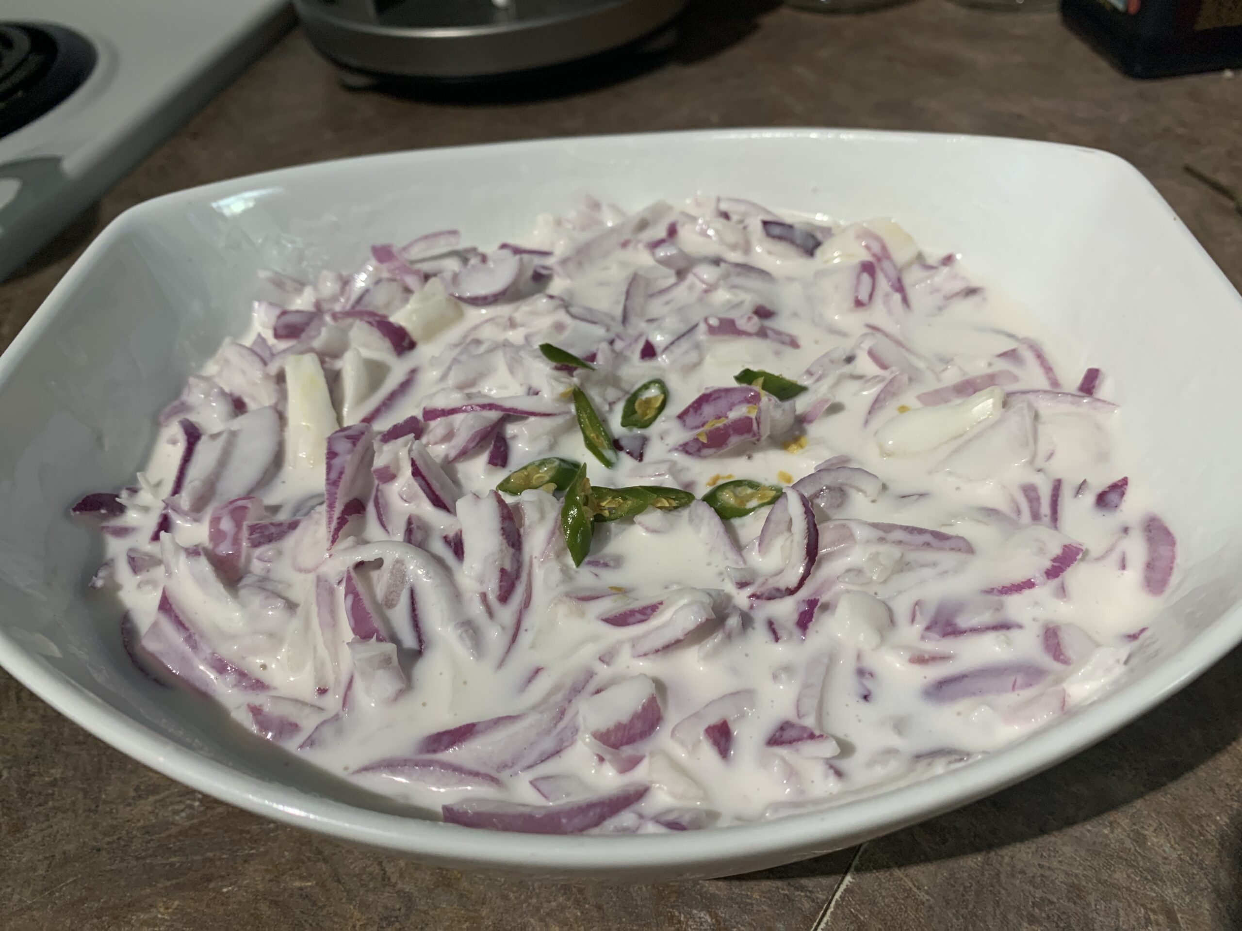A fresh red onion salad in a white bowl, featuring thinly sliced red onions, and a sprinkle of herbs, drizzled with lemon juice.