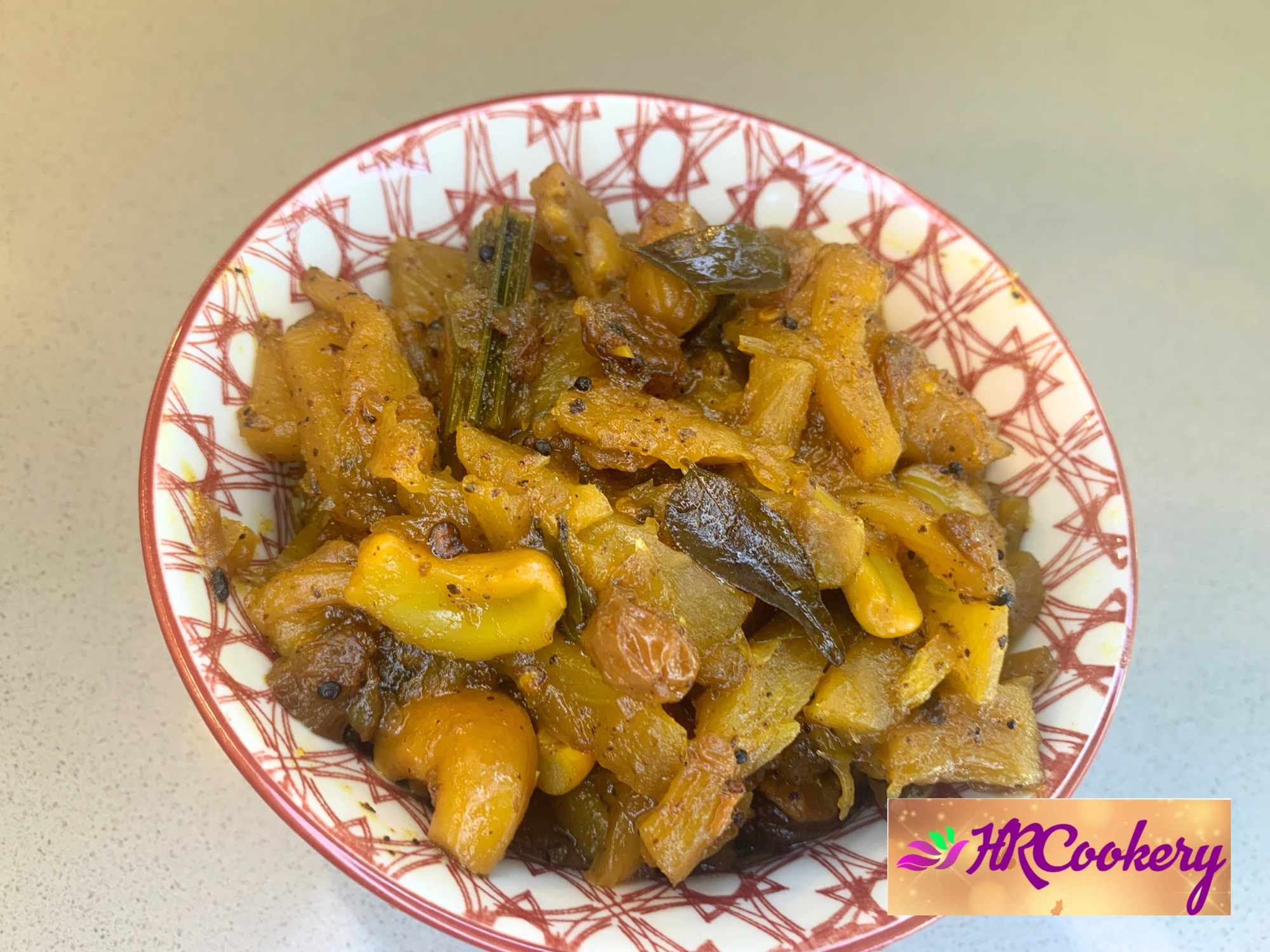 A glass jar of homemade pineapple chutney with chunks of pineapple and spices, sitting on a wooden surface next to a bowl of crackers.
