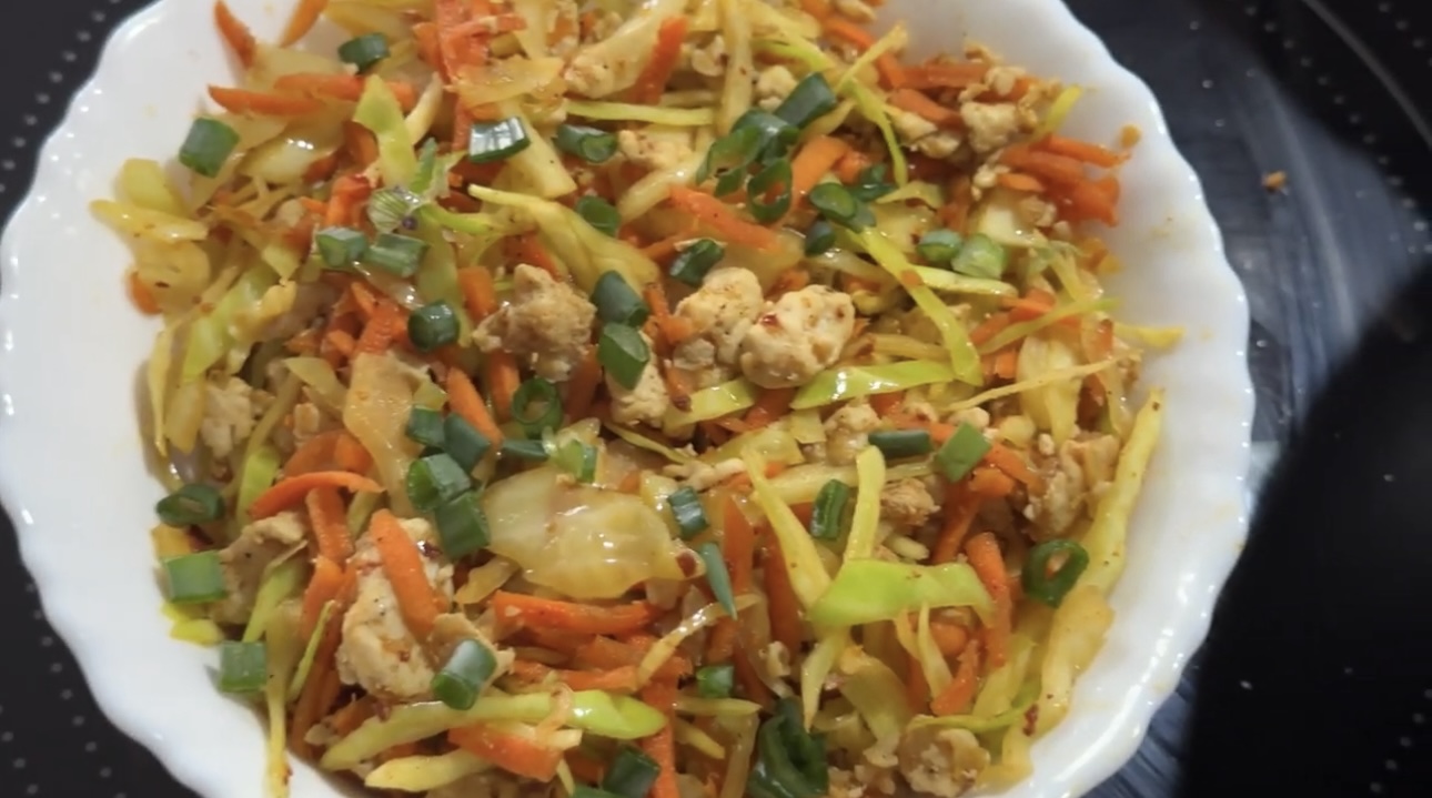 A colorful bowl of egg roll in a bowl, featuring ground meat, shredded cabbage, carrots, and green onions, garnished with sesame seeds.