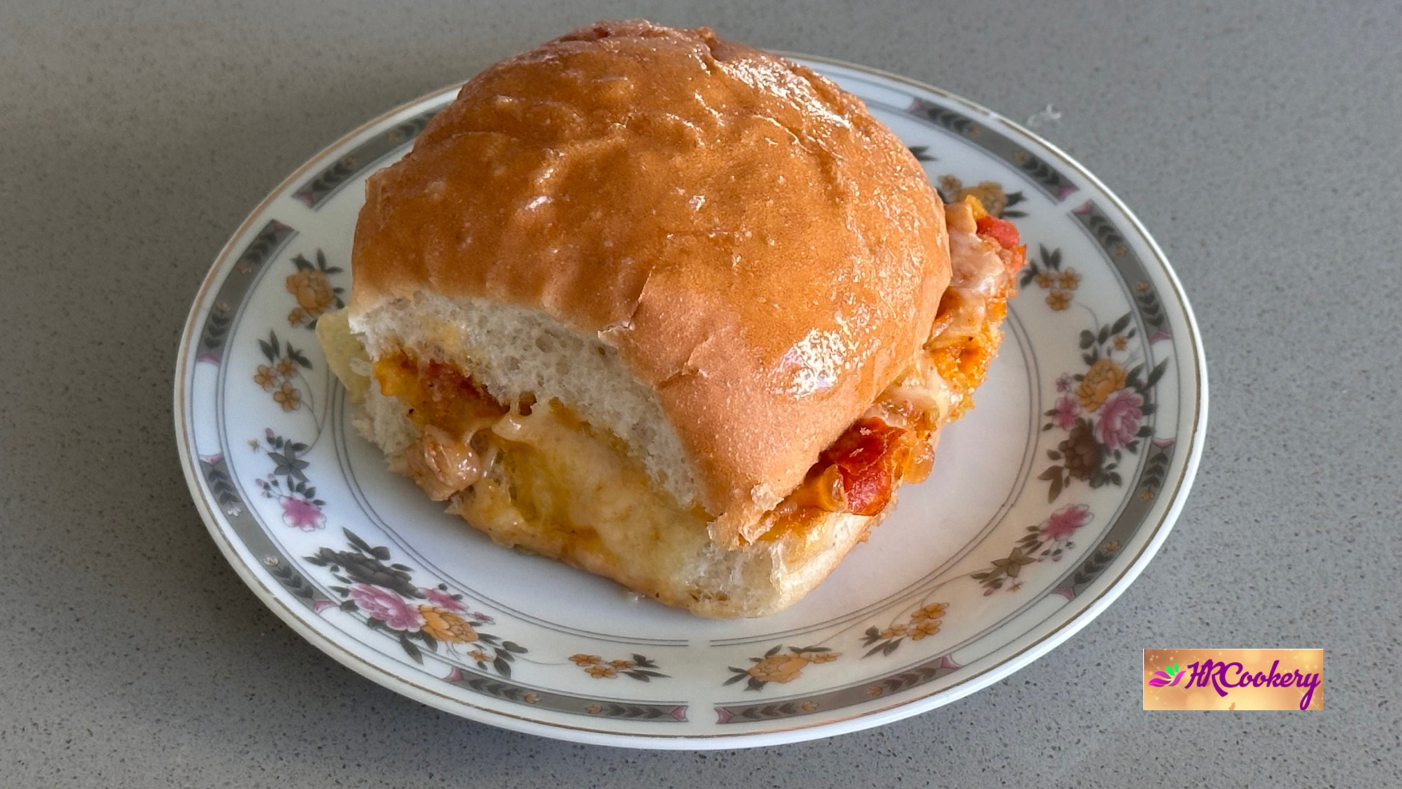 A soft bread roll filled with cheesy chicken on a floral-patterned plate.