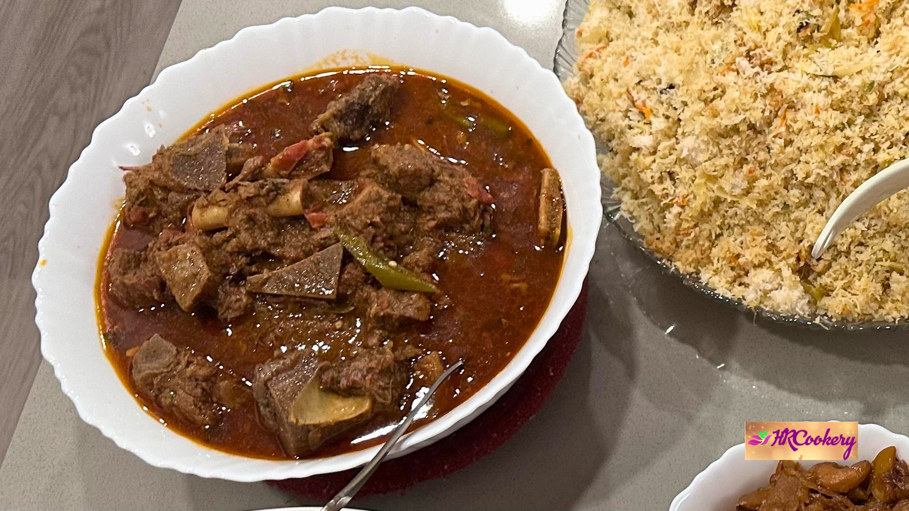 Close-up of a bowl of homemade Beef Karahi with tender bone-in beef simmered in a rich tomato-based gravy, served alongside a platter of Sri Lankan fried rice.